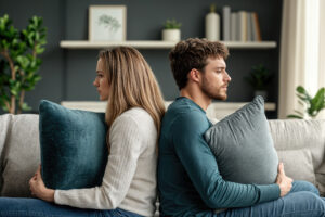 Upset young couple sitting back to back on sofa after argument at home.