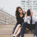 Woman comforting her upset boyfriend on city steps, showing empathy, forgiveness, and emotional connection.