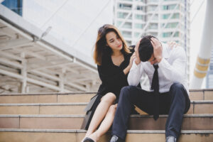 Woman comforting her upset boyfriend on city steps, showing empathy, forgiveness, and emotional connection.