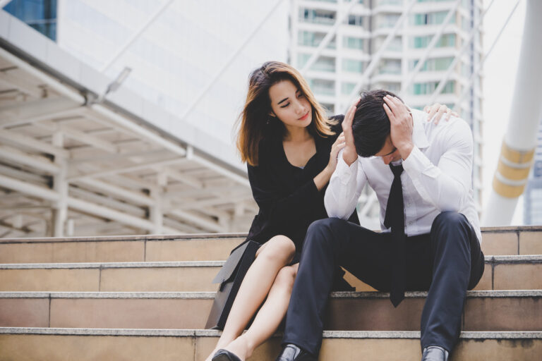 Woman comforting her upset boyfriend on city steps, showing empathy, forgiveness, and emotional connection.