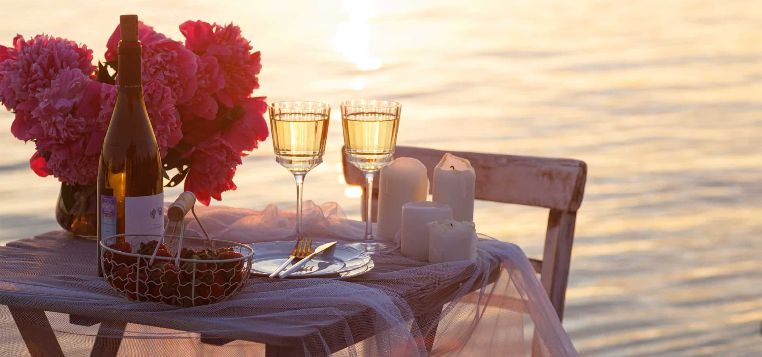 Romantic sunset waterfront table with champagne, flowers, and golden light for an intimate celebration.